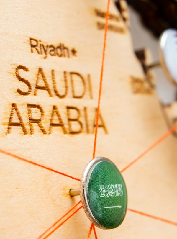 Saudi Arabia flag on the pushpin and red threads on the wooden map